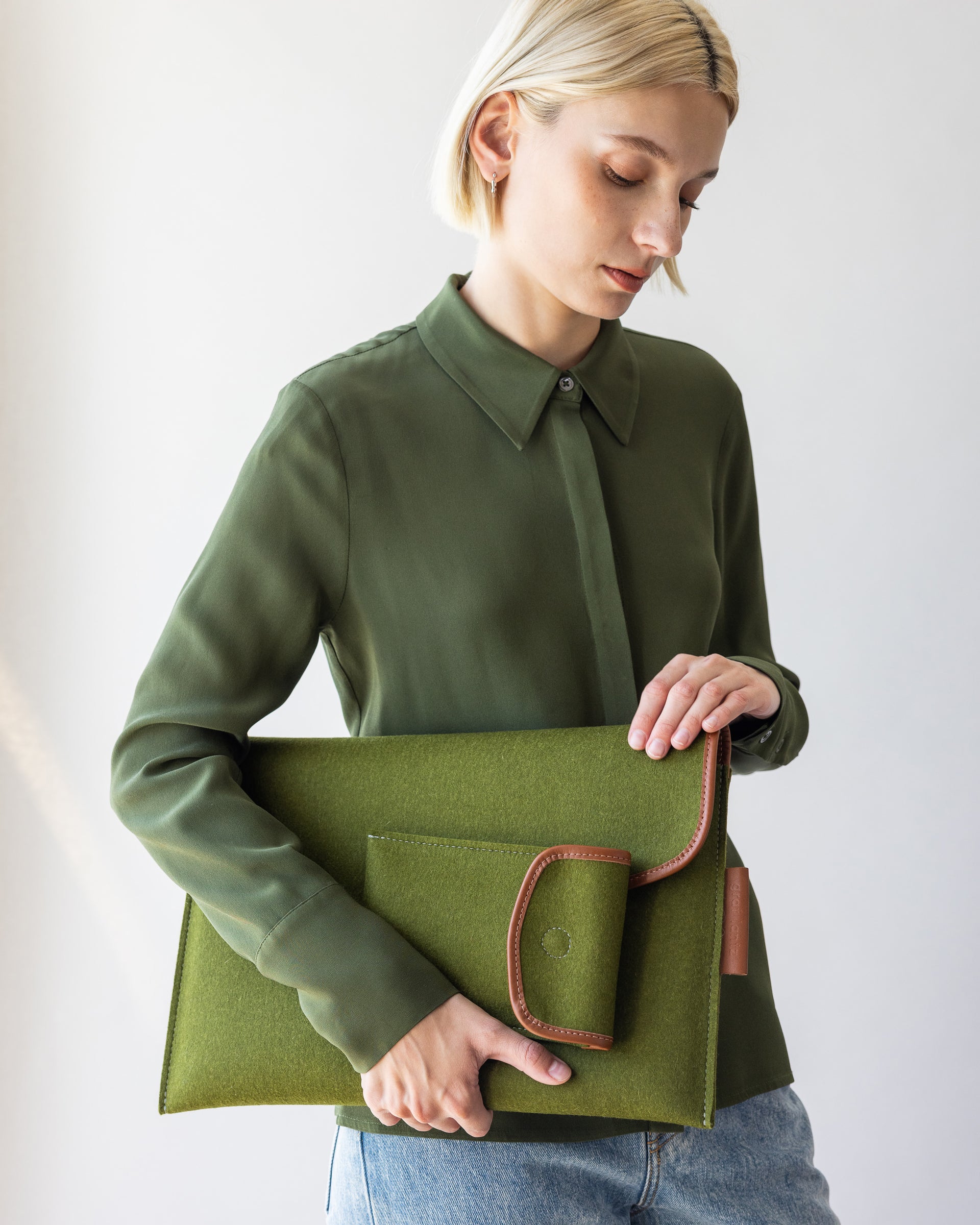 Envelope Merino Wool 16" Tech Sleeve and Envelope Accessory Sleeve in green held by a stylish woman in one hand by her side