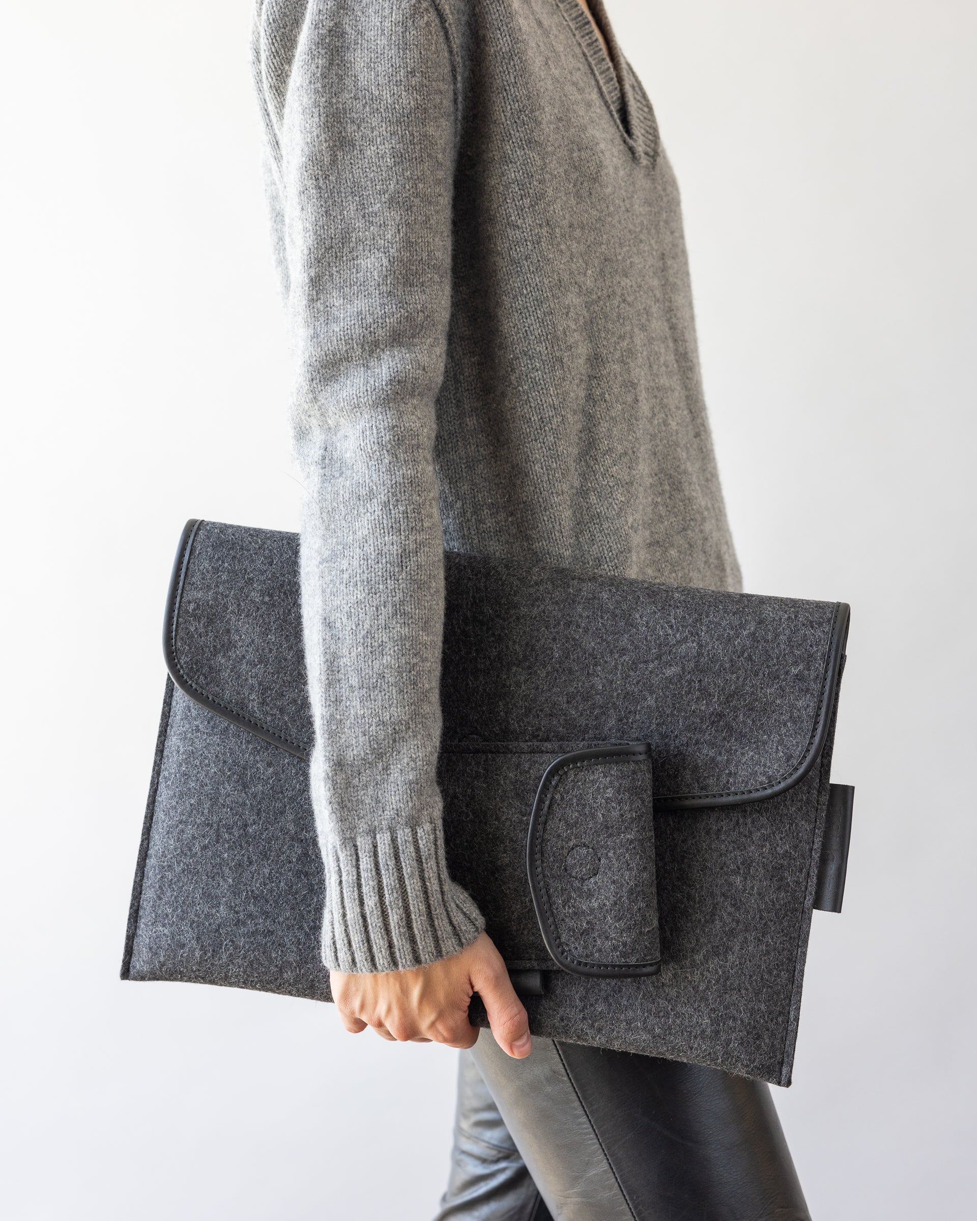 Envelope Merino Wool Tech Sleeve and Envelope Accessory Sleeve in charcoal held by a stylish woman in one hand by her side