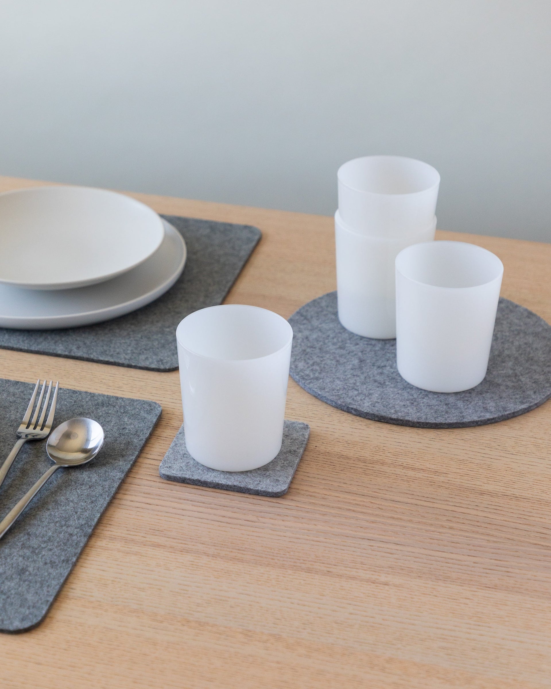 Table setting with gray placemats, plates, silver cutlery and foam-colored drinking glasses on coasters and trivet