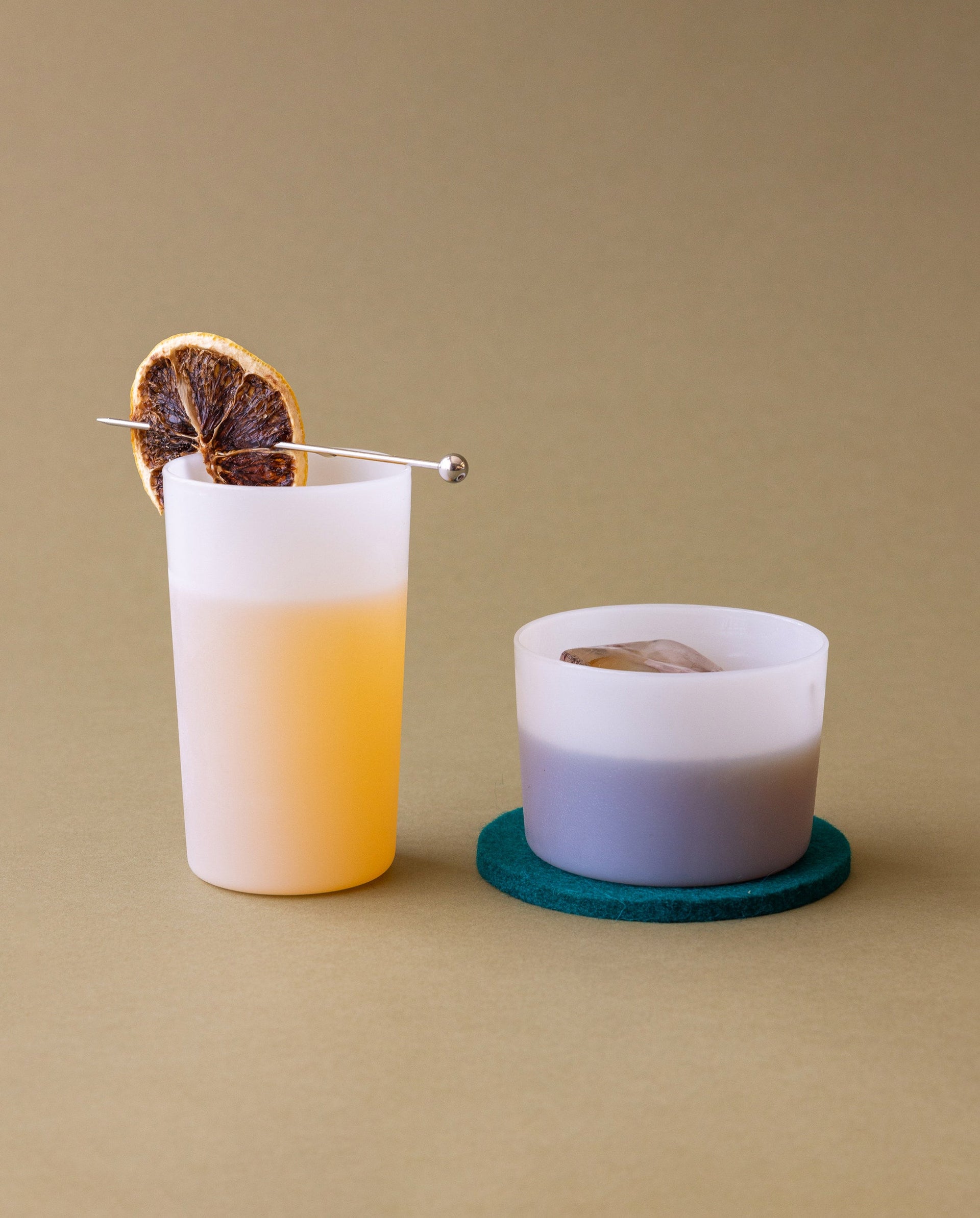 Two foam-colored filled drinking glasses with fruit-decoration by Graf Lantz, one on a Merino wool coaster