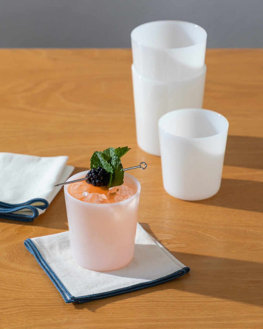 Four small glass tumblers in color foam on a wooden tabletop next to square folded napkins