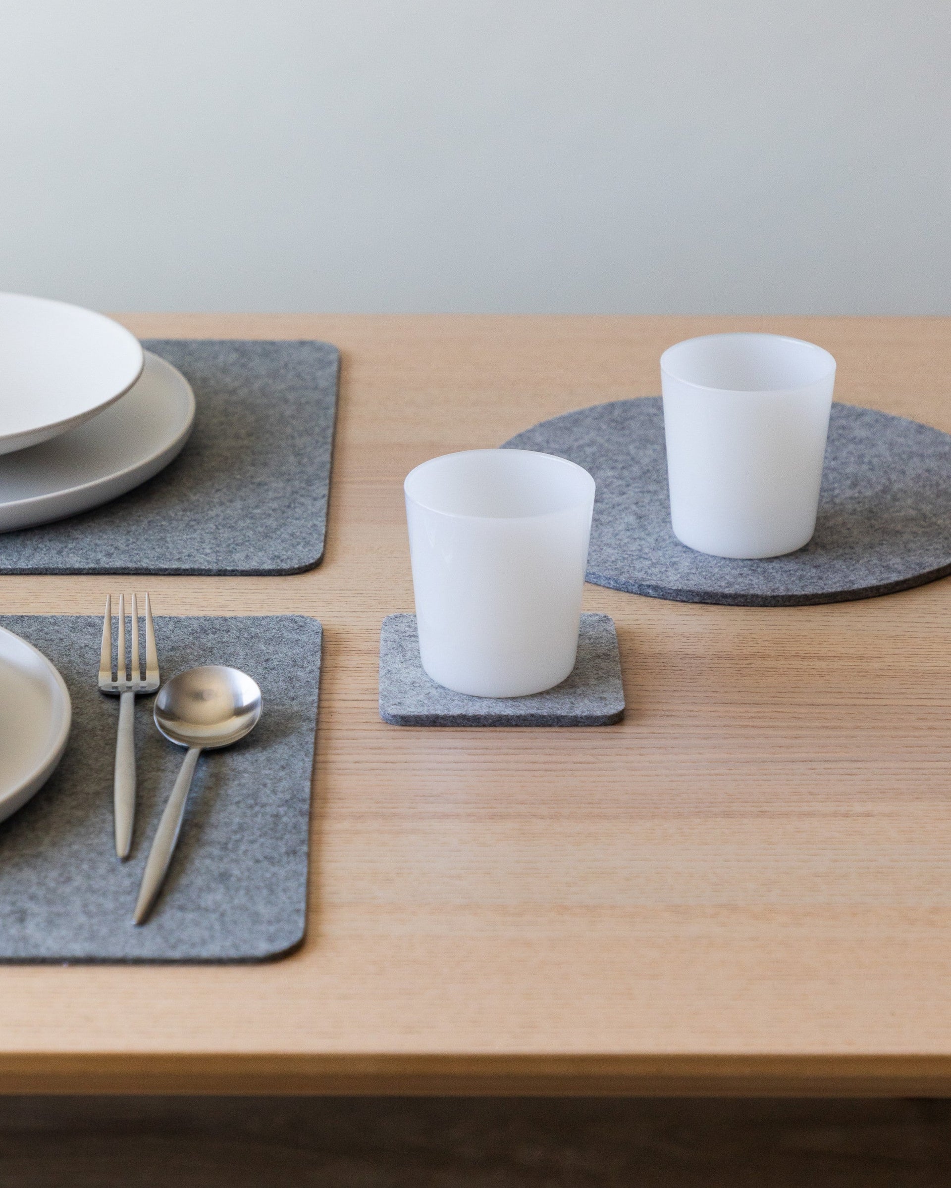 Table setting with gray placemats, plates, silver cutlery and foam-colored drinking glasses on coaster and trivet