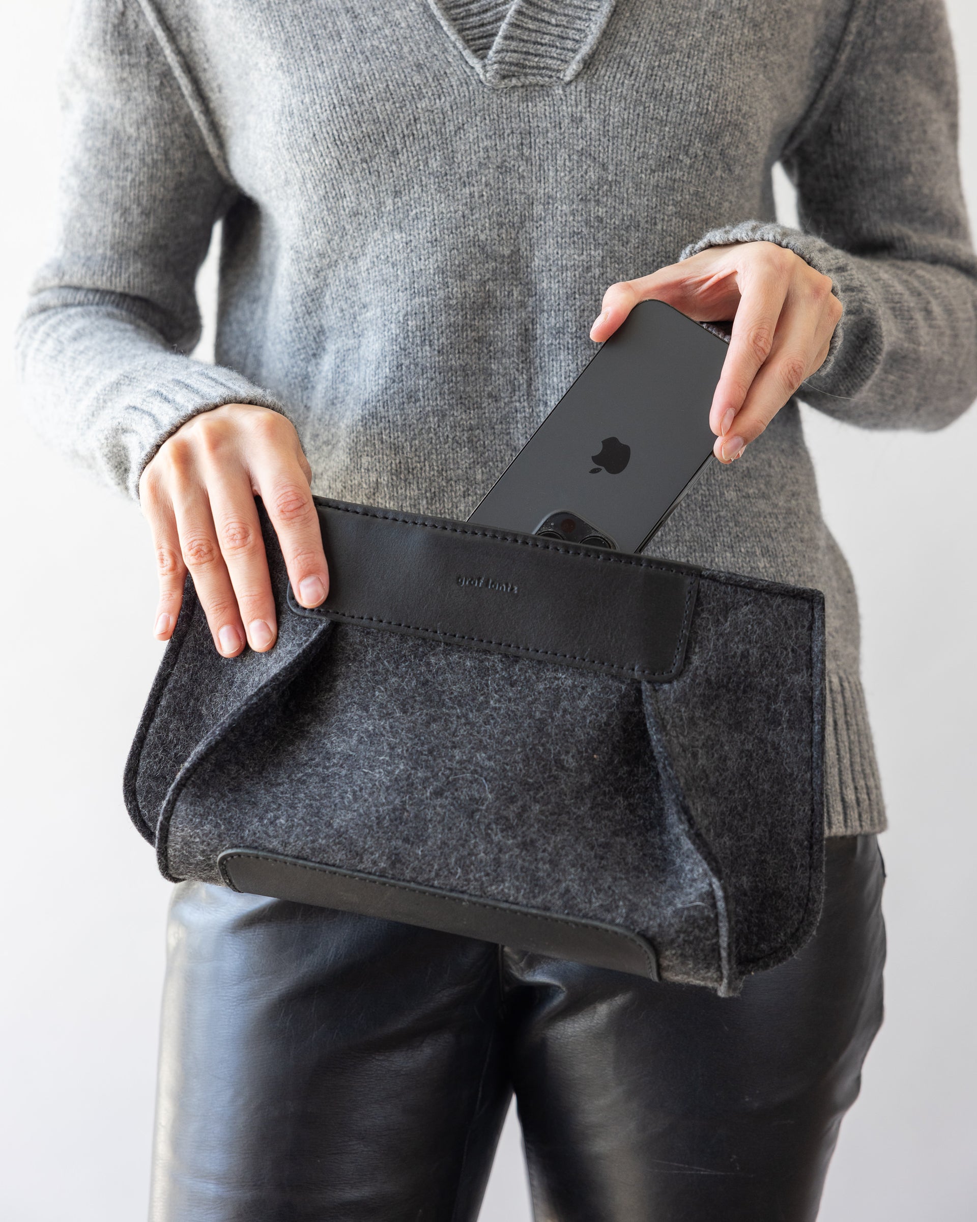 A woman taking a mobile phone out of a charcoal Frankie Merino Wool Clutch 