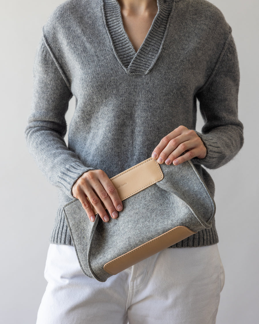 A gray Frankie Merino Wool Clutch held by a stylish woman in her hands, front view