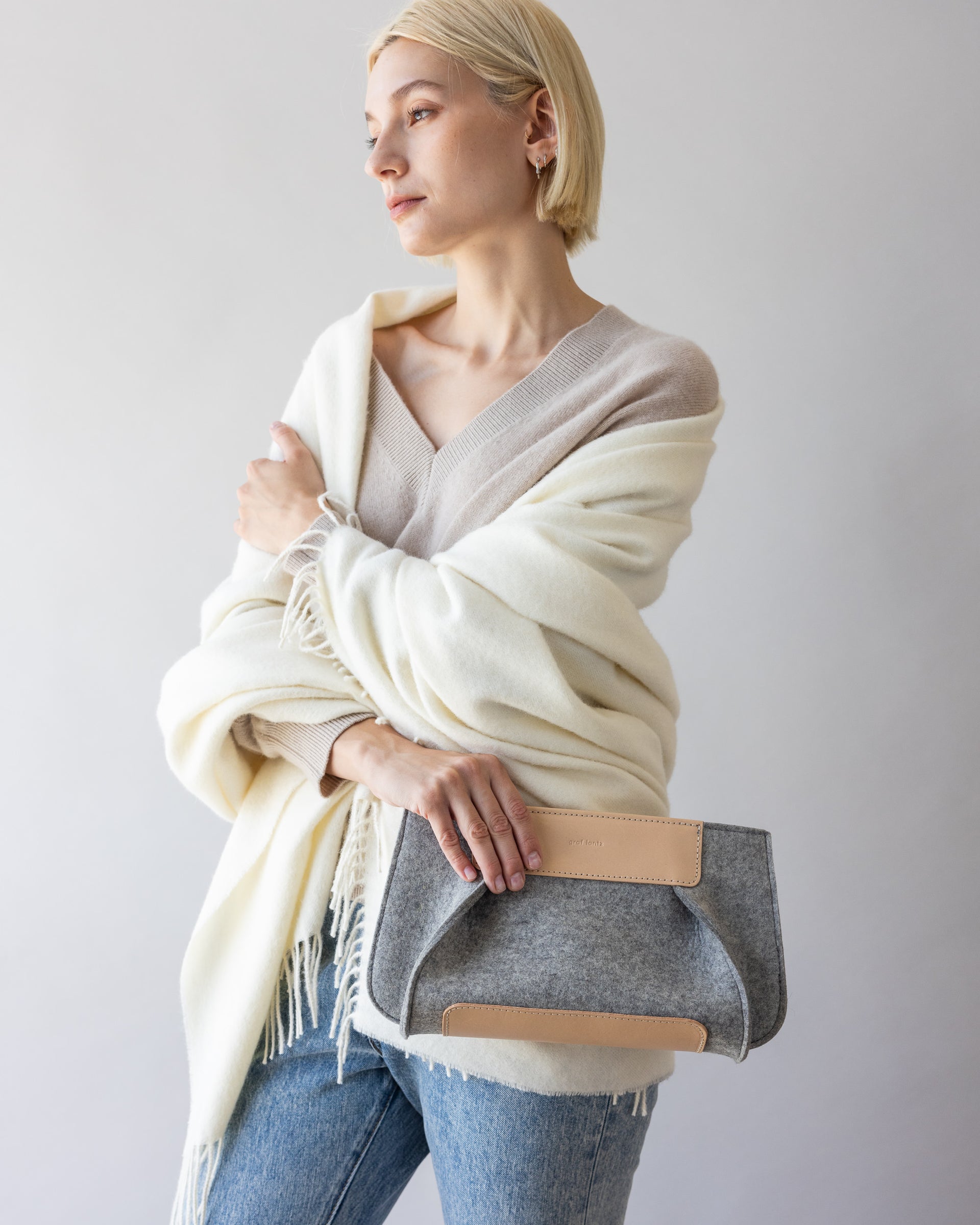 A woman with white throw holding a Frankie Merino Wool Clutch in one hand by her side