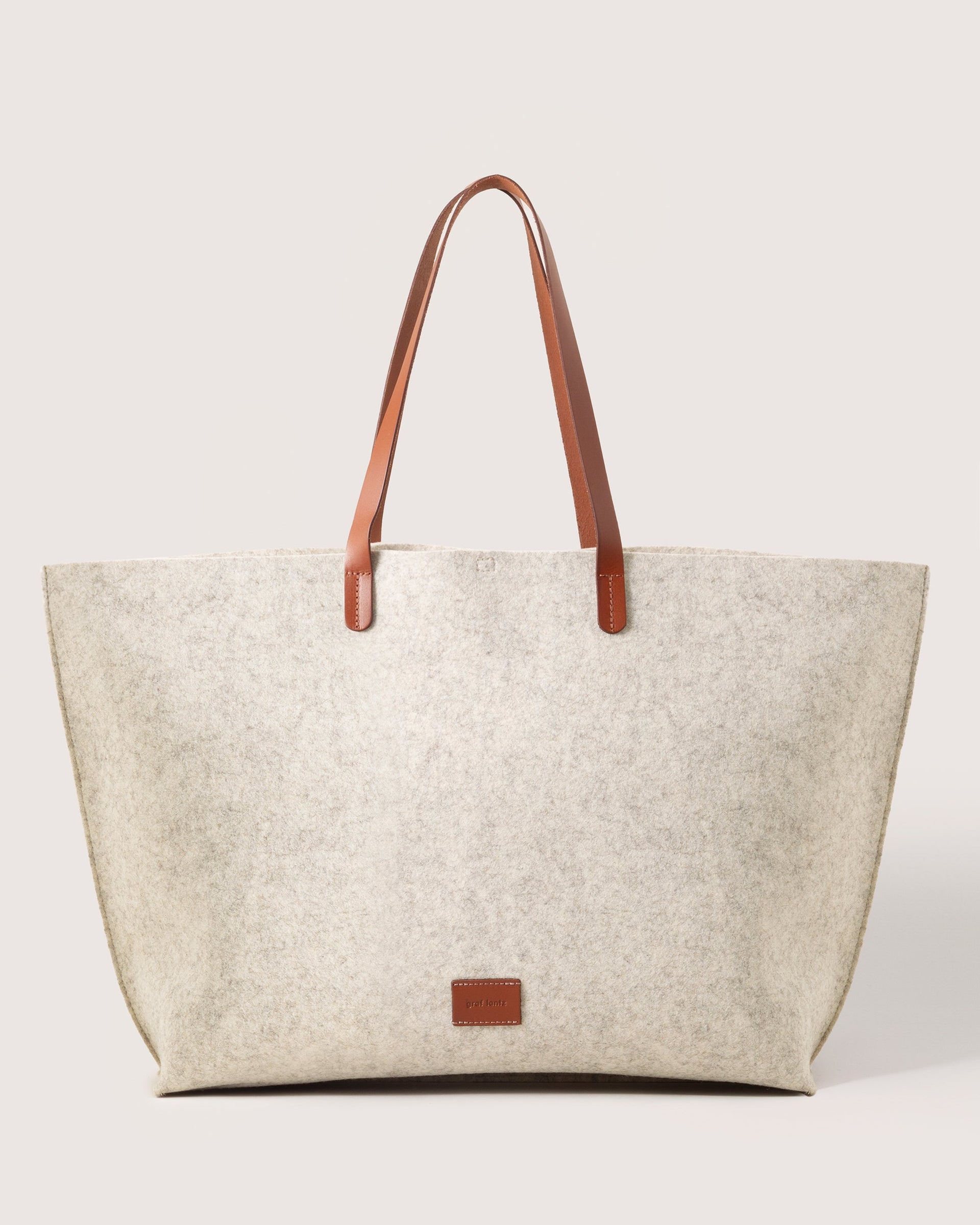 Heather white Hana Merino Wool Boat Bag with brown leather handles and brand logo, front view, white background.