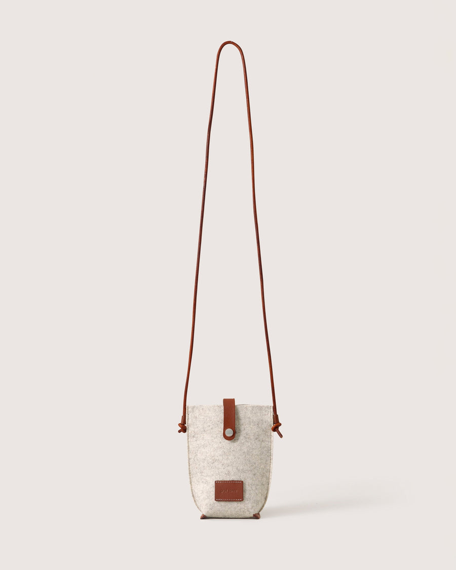 Heather white Hana Merino Wool Phone Crossbody with dark brown leather strap, brand label, and snap closure, white background. 