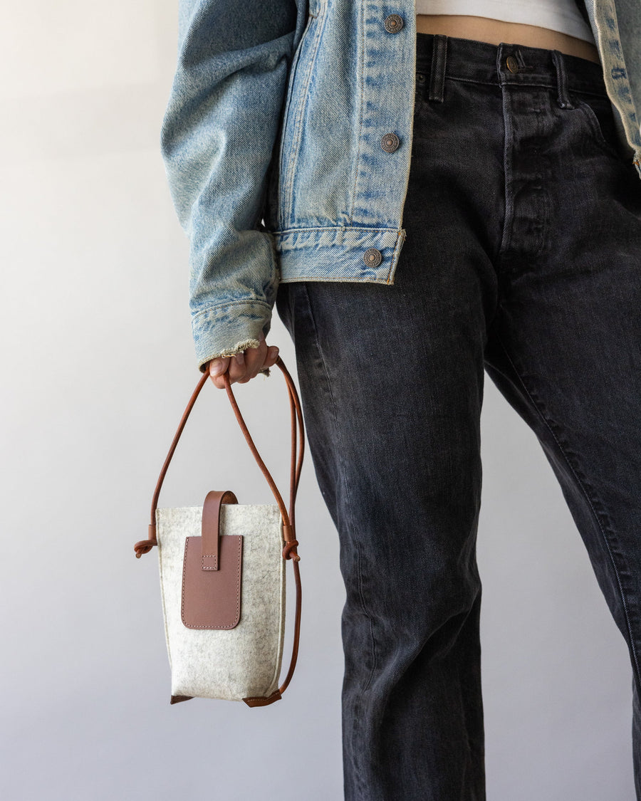 Woman holds dark brown leather strap of Graf Lantz' Hana Merino Wool Phone Crossbody in one hand by her side, backside of the bag visible.