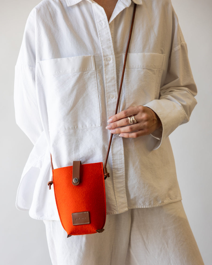 Orange Hana Merino Wool Phone Crossbody diagonally across a woman's body, with the strap over one shoulder and the bag resting on the opposite hip.