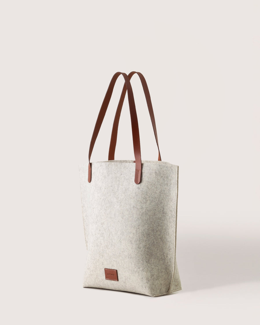 White Hana Merino Wool Tote by Graf Lantz featuring brown leather handles and leather logo tag, side view, white background.