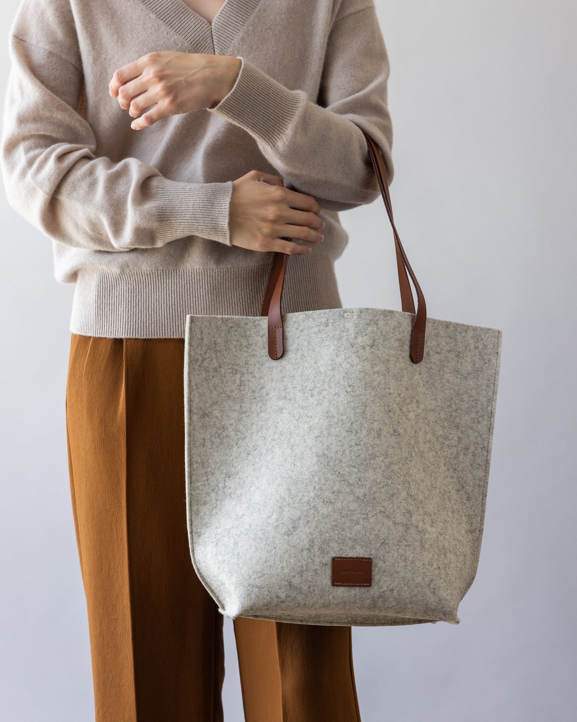 Standing woman with brown leather straps of white Hana Merino Wool Tote over one arm.