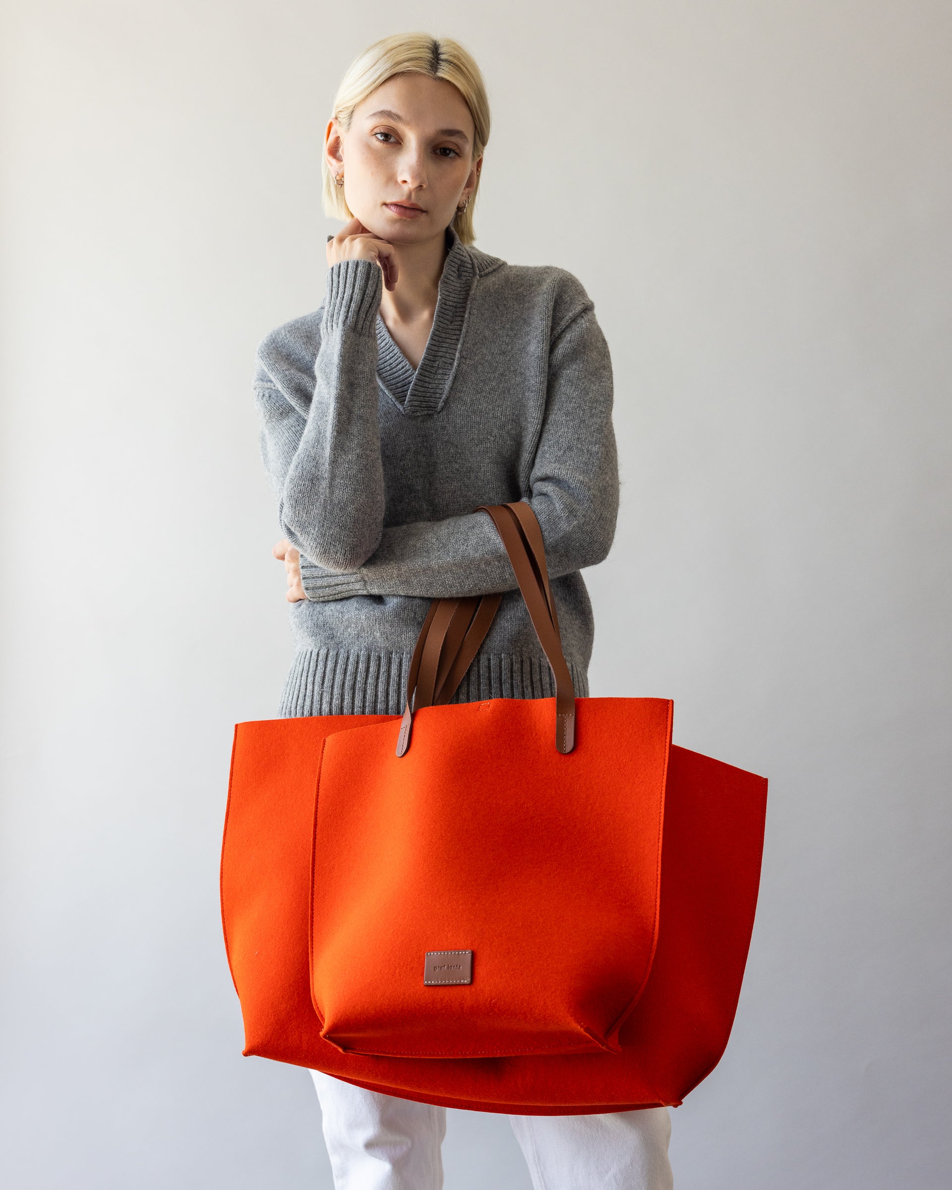 Merino Wool Boat bag behind orange smaller Merino Wool Tote bag both with sienna brown handles over a woman's arm