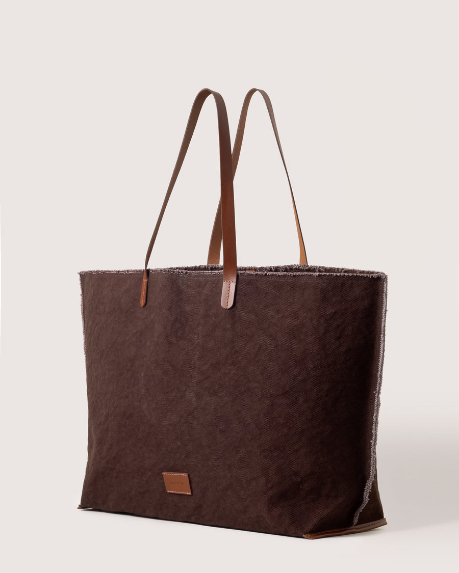 A dark brown Hana Canvas Boat Bag with dark brown leather handle, white background, side view