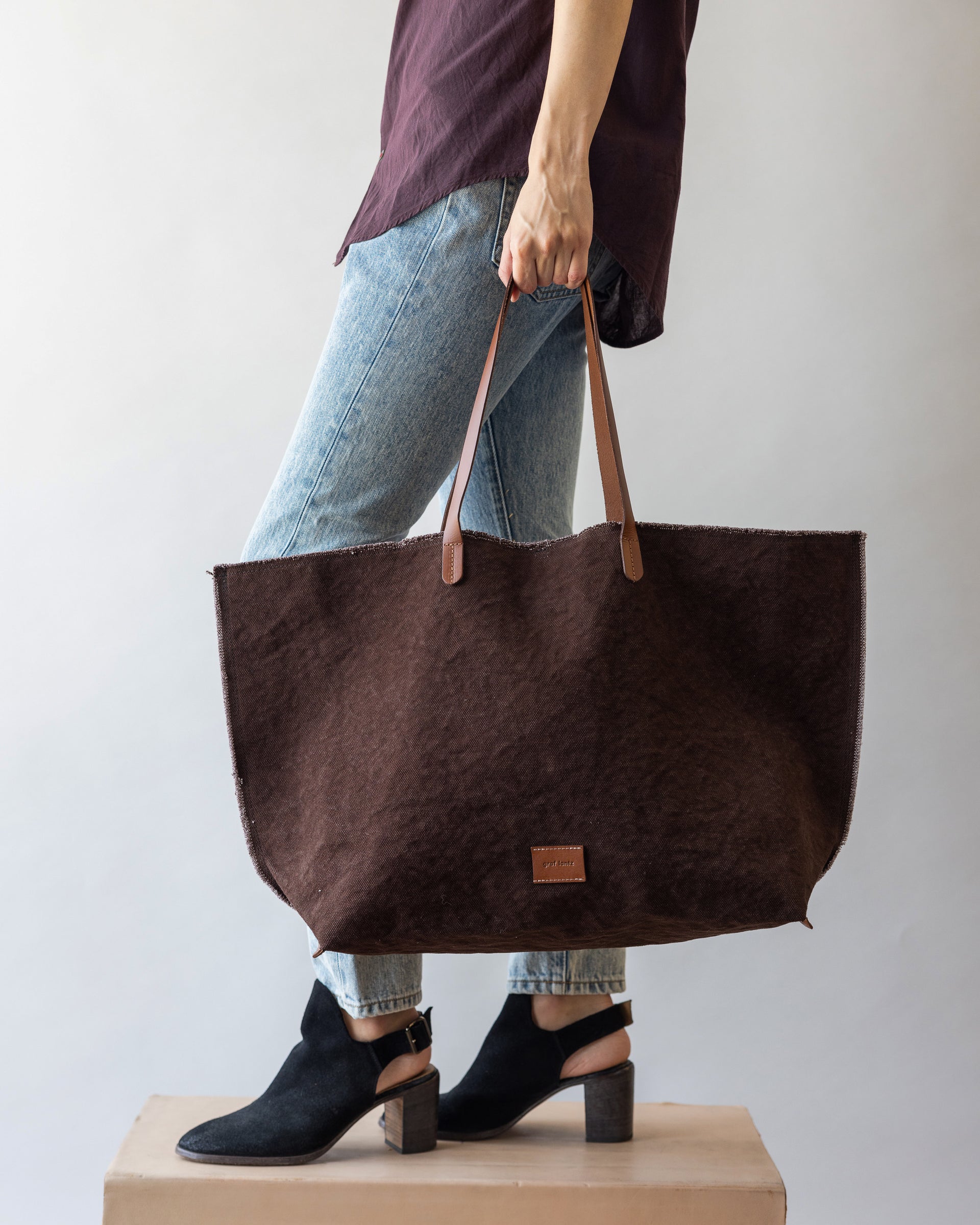A woman holding a Hana Canvas Boat Bag by Graf Lantz in Deep Brown Sienna on the dark brown leather handle