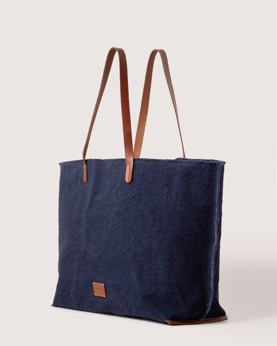 A dark blue Hana Canvas Boat Bag with dark brown leather handle, white background, side view