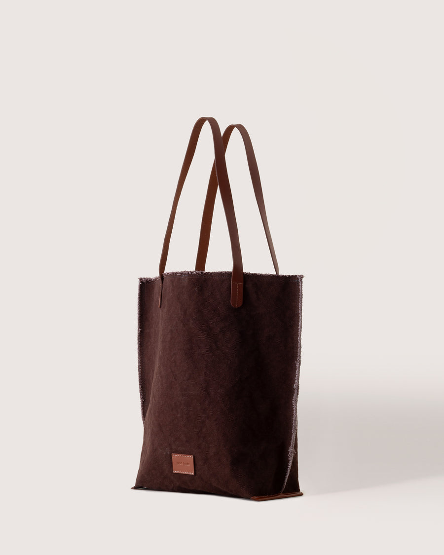 A dark brown Hana Canvas Tote with dark brown leather handle, white background, side view