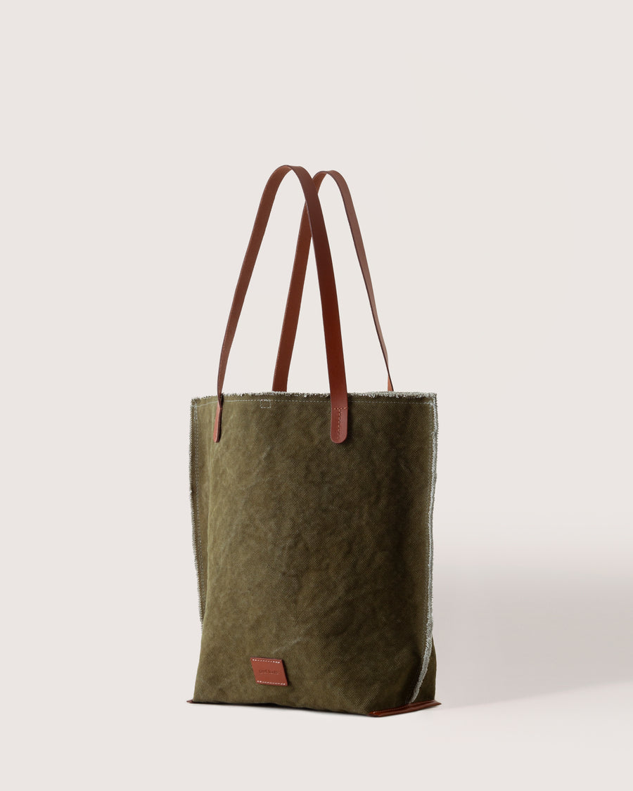A dark green Hana Canvas Tote with dark brown leather handle, white background, side view