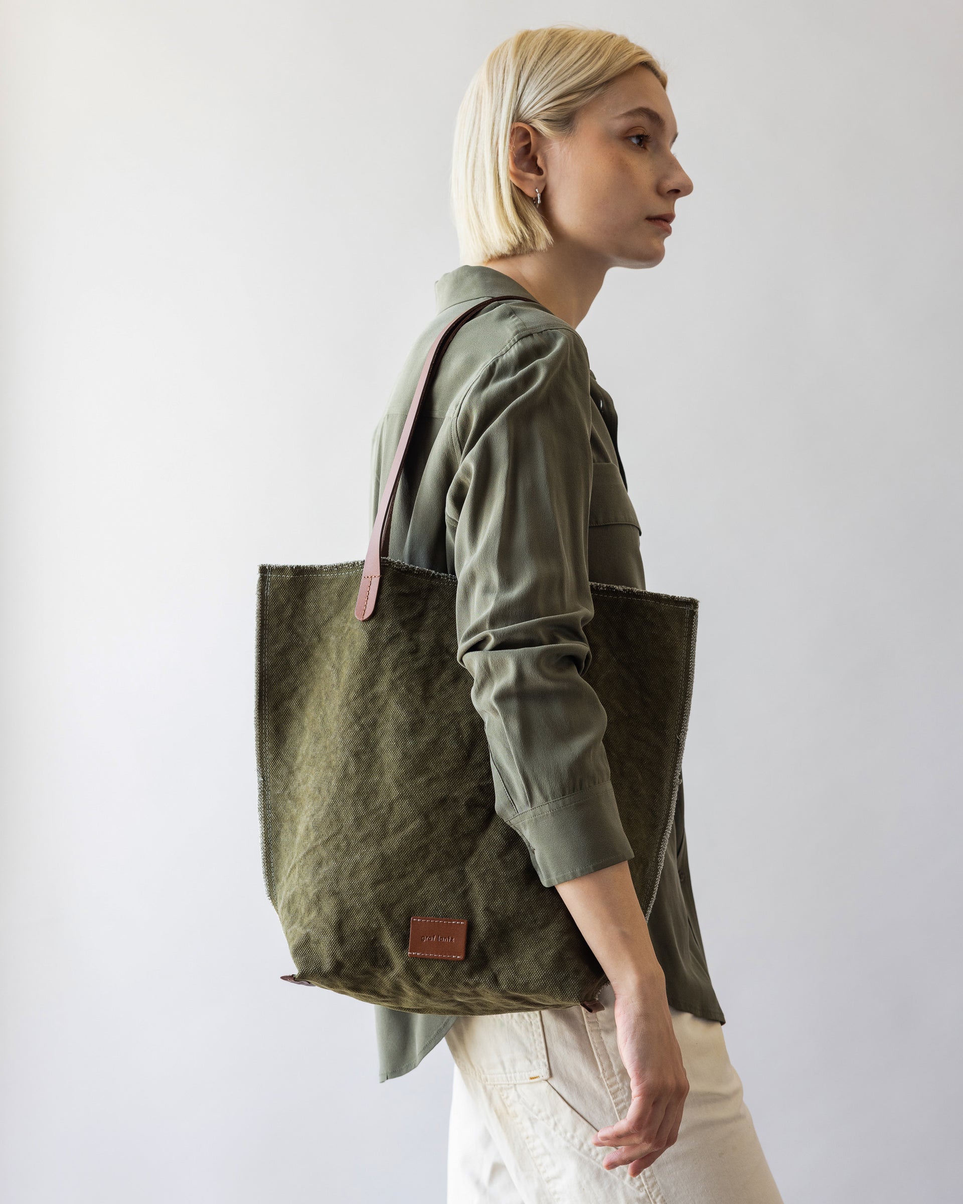 A blonde woman carrying a green Hana Canvas Tote over her shoulder 