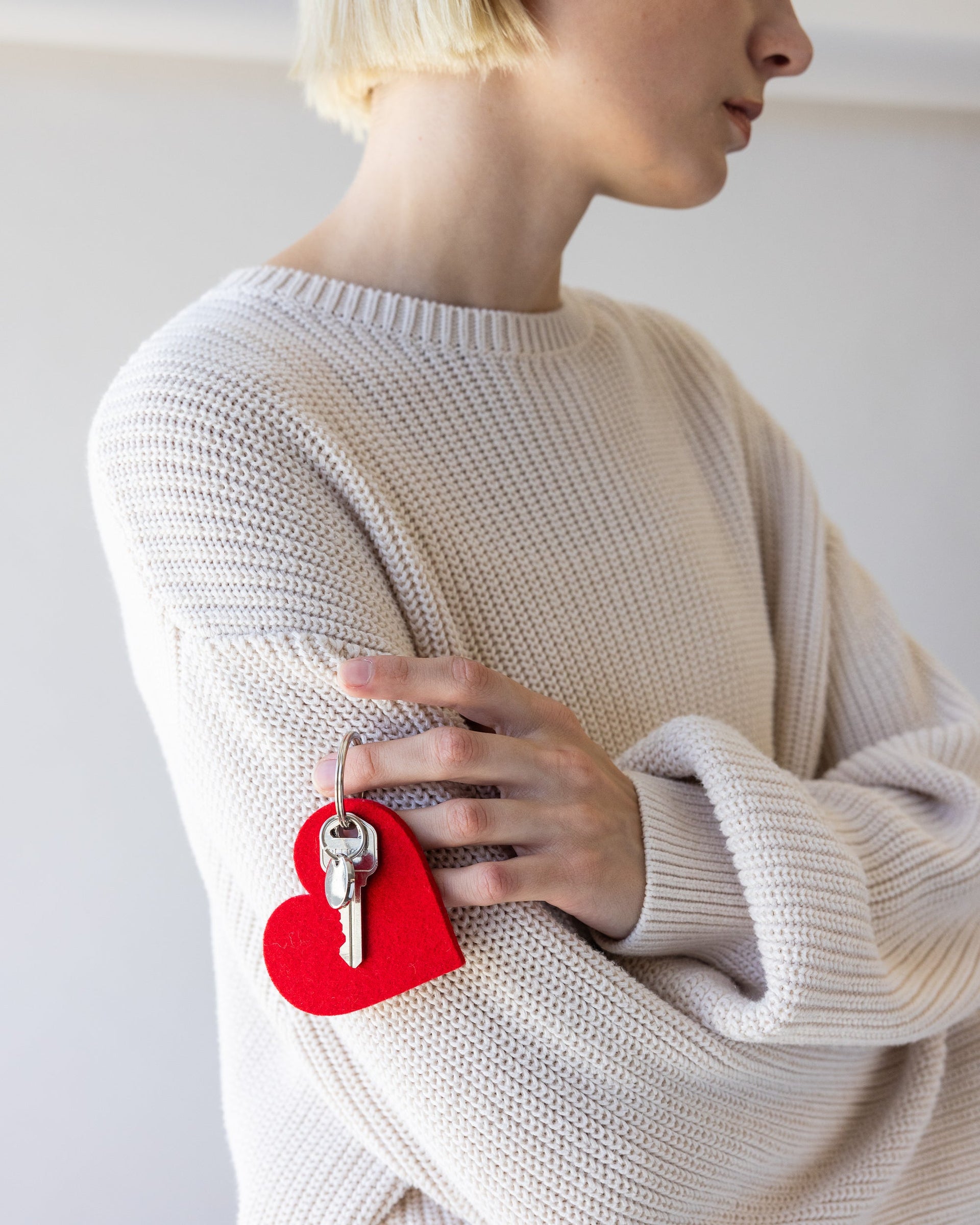 A woman with crossed arms has a Heart Merino Wool Felt Key Fob in red in one hand, side view