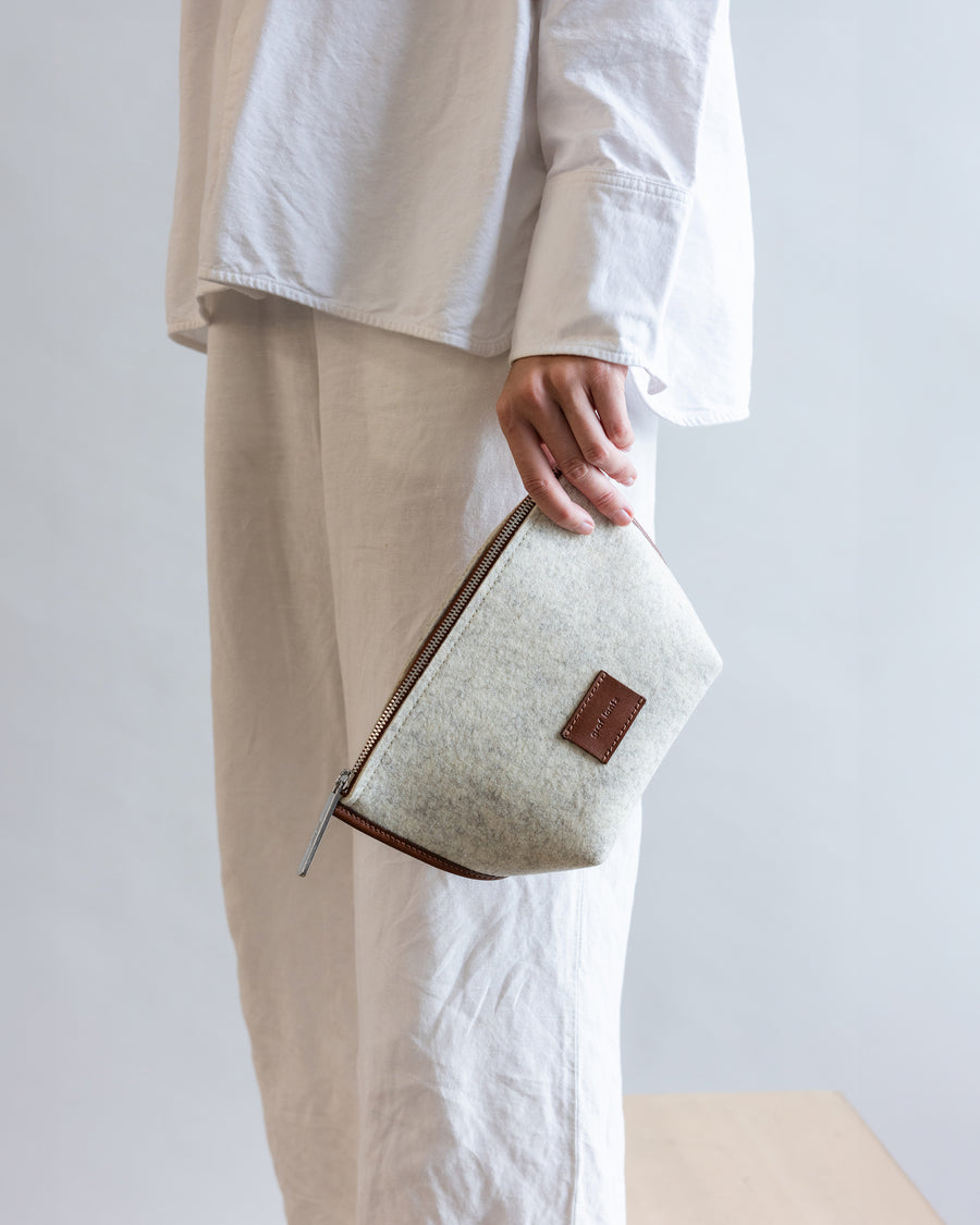 Standing woman holds Heather  White Hana Merino Wool Pouch with one hand by her side