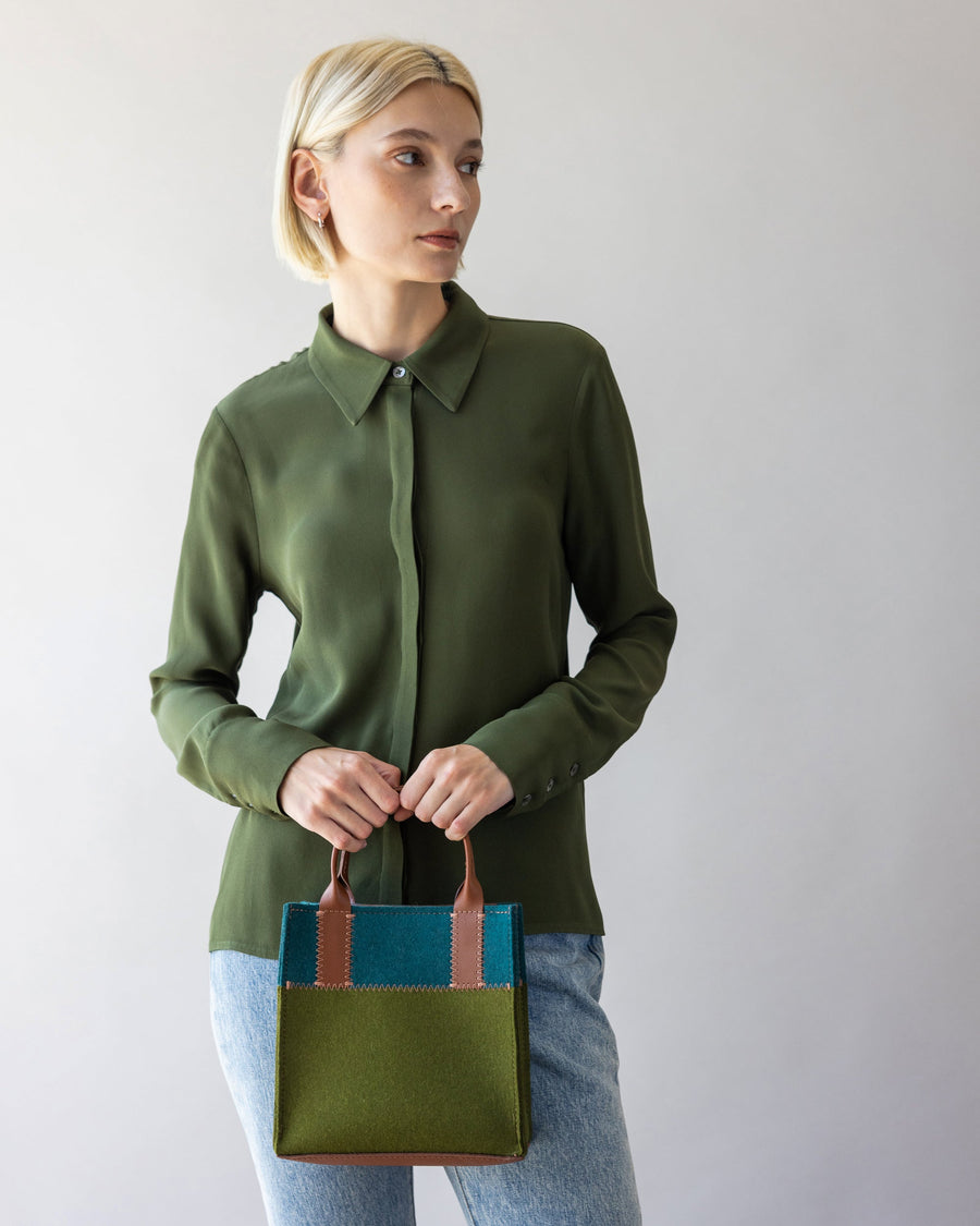 Standing woman holds Moss and Kombu colored Jaunt Merino Wool Mini Tote with both side in front of her, white background