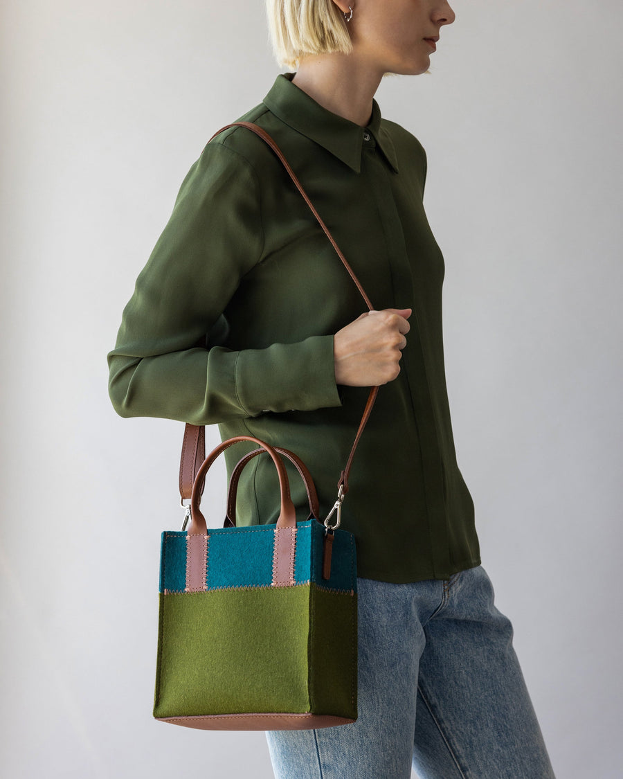 Brown leather shoulder strap of Moss and Kombu colored Jaunt Merino Wool Mini Tote over a woman's shoulder, side view, white background