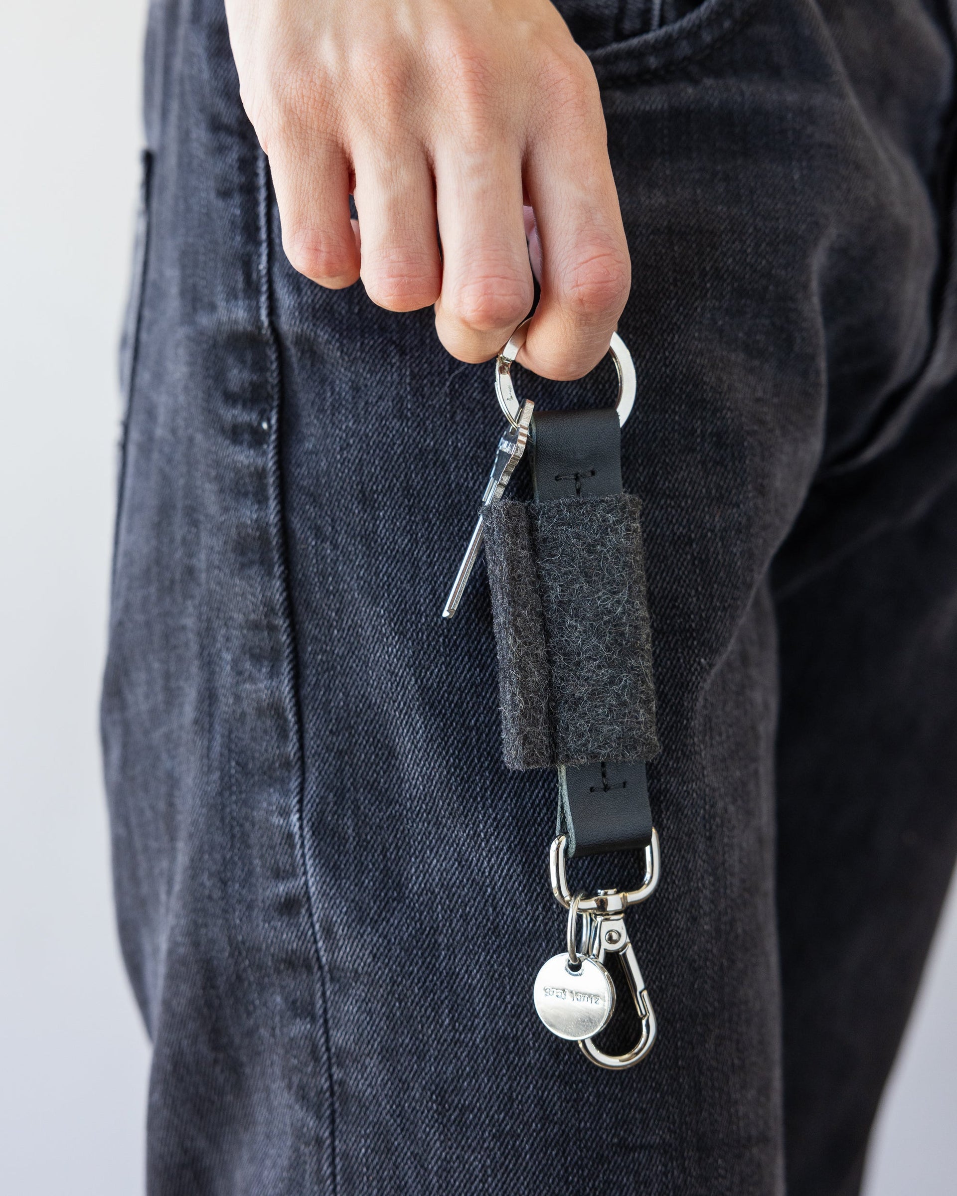Standing woman holds Charcoal Merino Wool Bar Key Fob on one finger next to her leg wearing black jeans