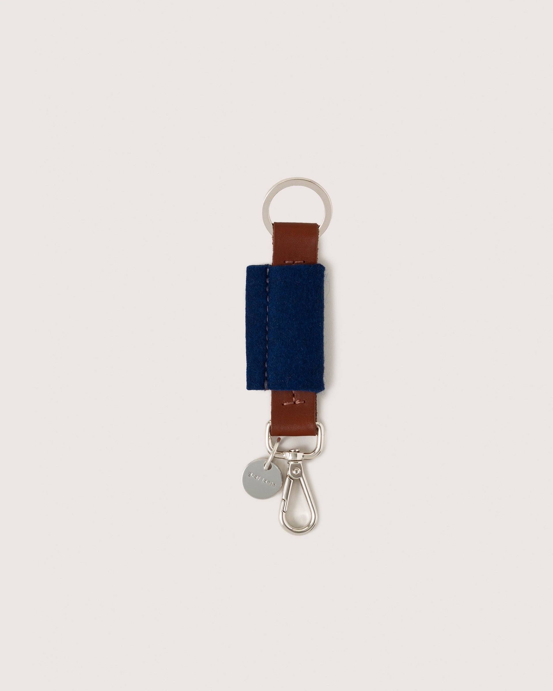 Merino Wool Bar Key Fob in blue with silver colored key ring, lobster clasp, and brand logo in brown leather, white background.