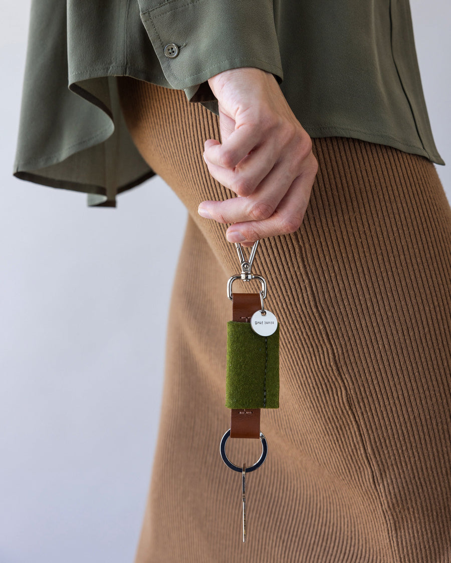 Standing woman holds Merino Wool Bar Key Fob by Graf Lantz in color Moss in one hand by her side, front view, white background