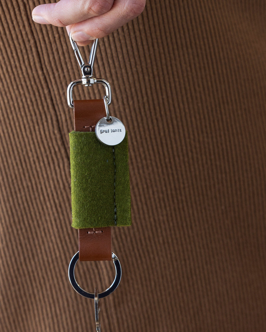 Woman holds green Merino Wool Bar Key Fob in one hand next to her side, close up