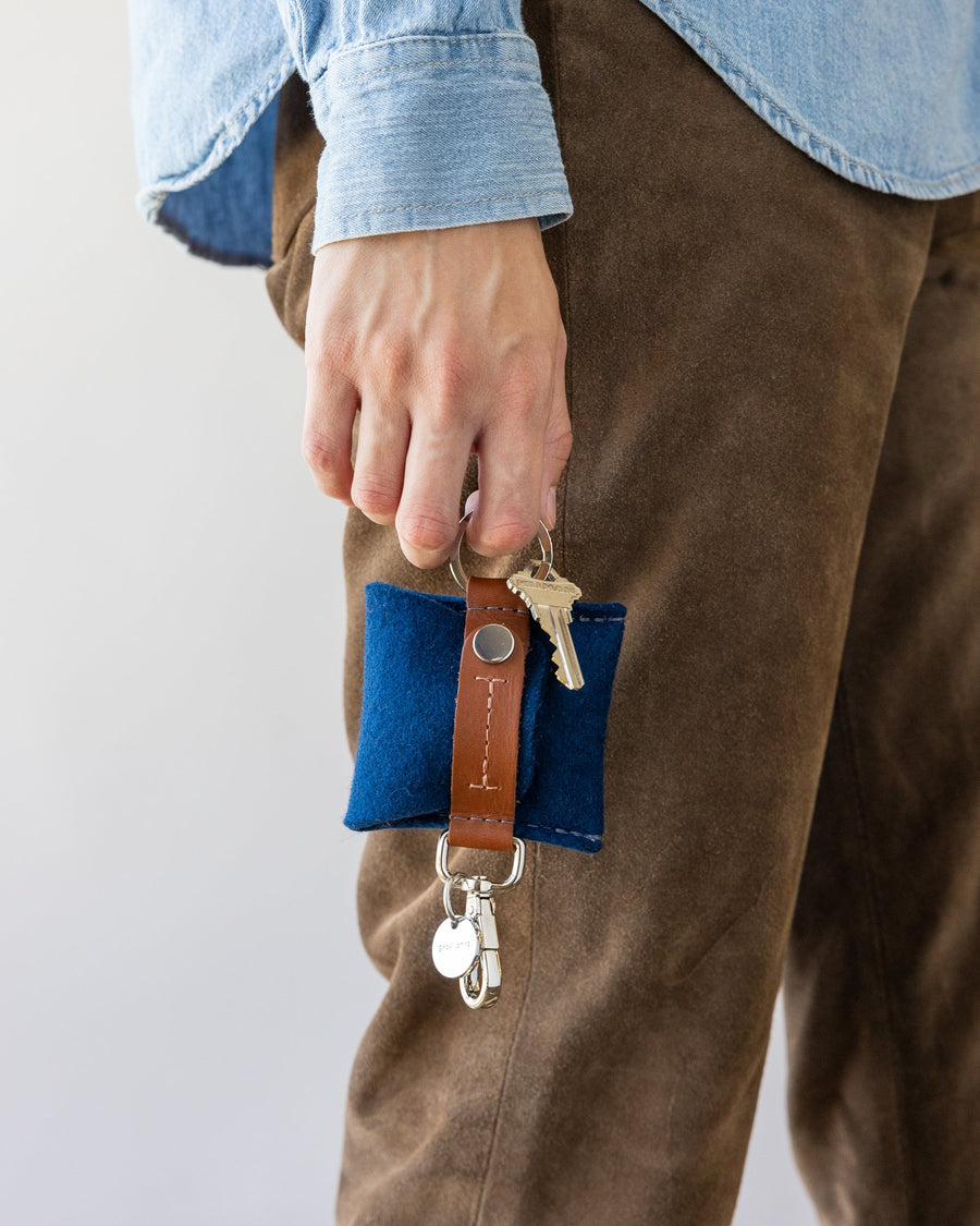 Standing woman holds blue Merino Wool Pod Key Fob with dark brown leather applications in hand by her side, side view.