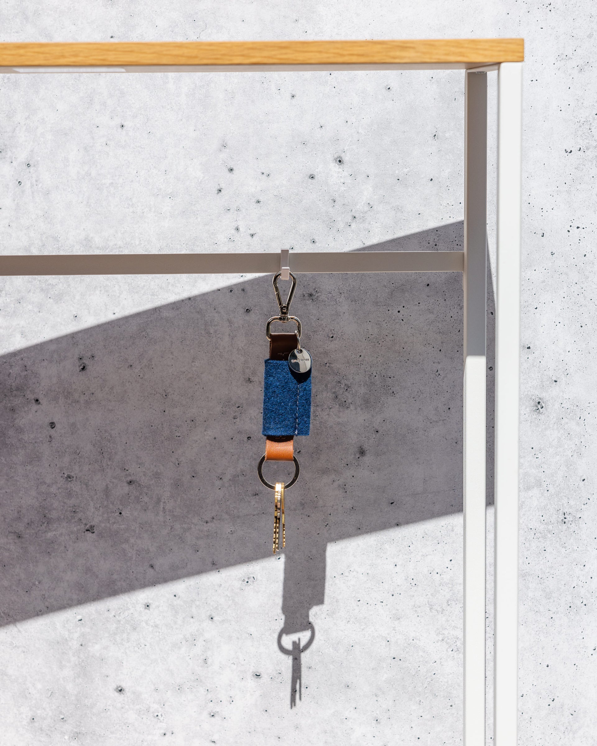 Merino Wool Bar Key Fob in blue with silver colored key ring with keys and  brown leather application hanging on a wardrobe in front of gray stone wall