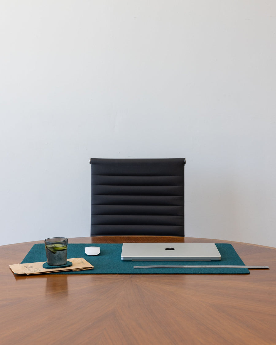 Office scene with office chair and wooden desk, on tabletop a Kombu Mosen Merino Wool Large Desk Pad with white laptop and mouse next to a green drinking glass