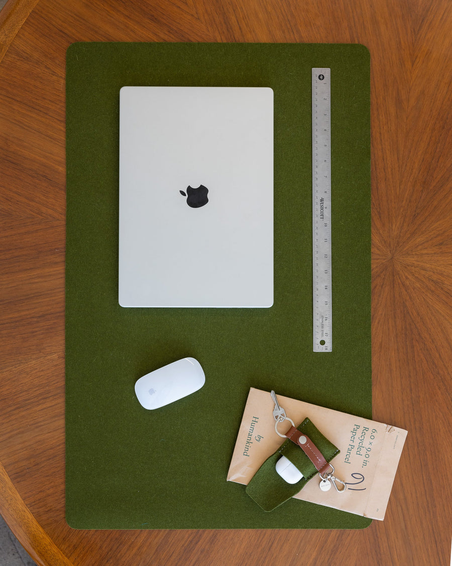 White laptop, mouse, and office accessories on Moss Mosen Merino Wool Large Desk Pad on a wooden tabletop