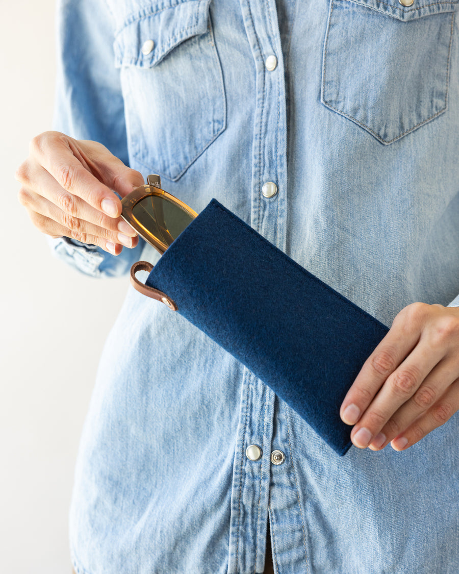 Woman putting a pair of brown sunglasses into a Merino Wool Felt Eyeglass Sleeve in marine color 