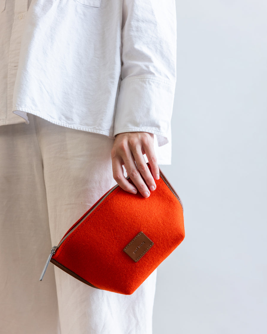 Standing woman holds orange Hana Merino Wool Pouch with one hand by her side