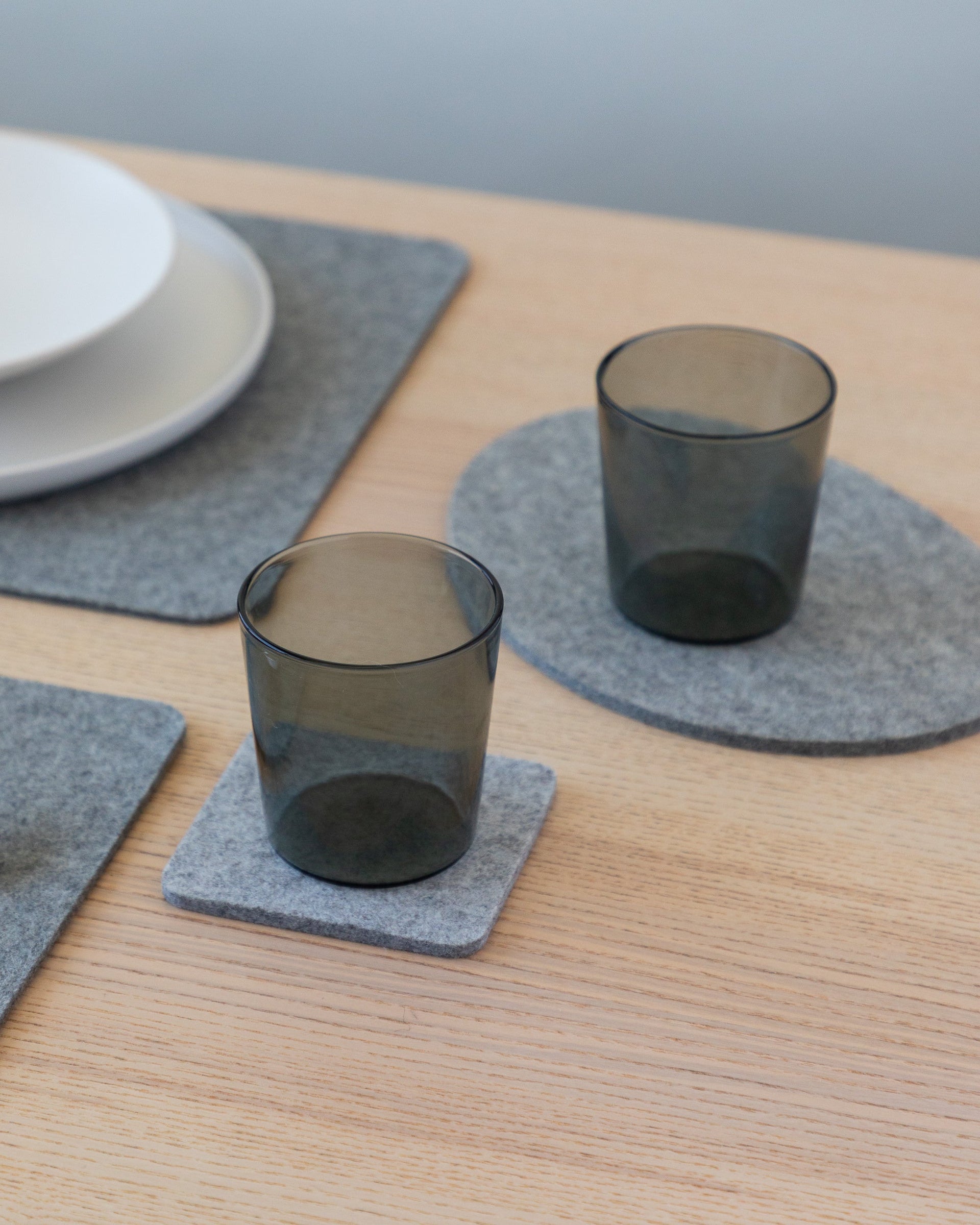 Table setting with gray placemats, plates, silver cutlery and smoke-colored drinking glasses on coaster and trivet