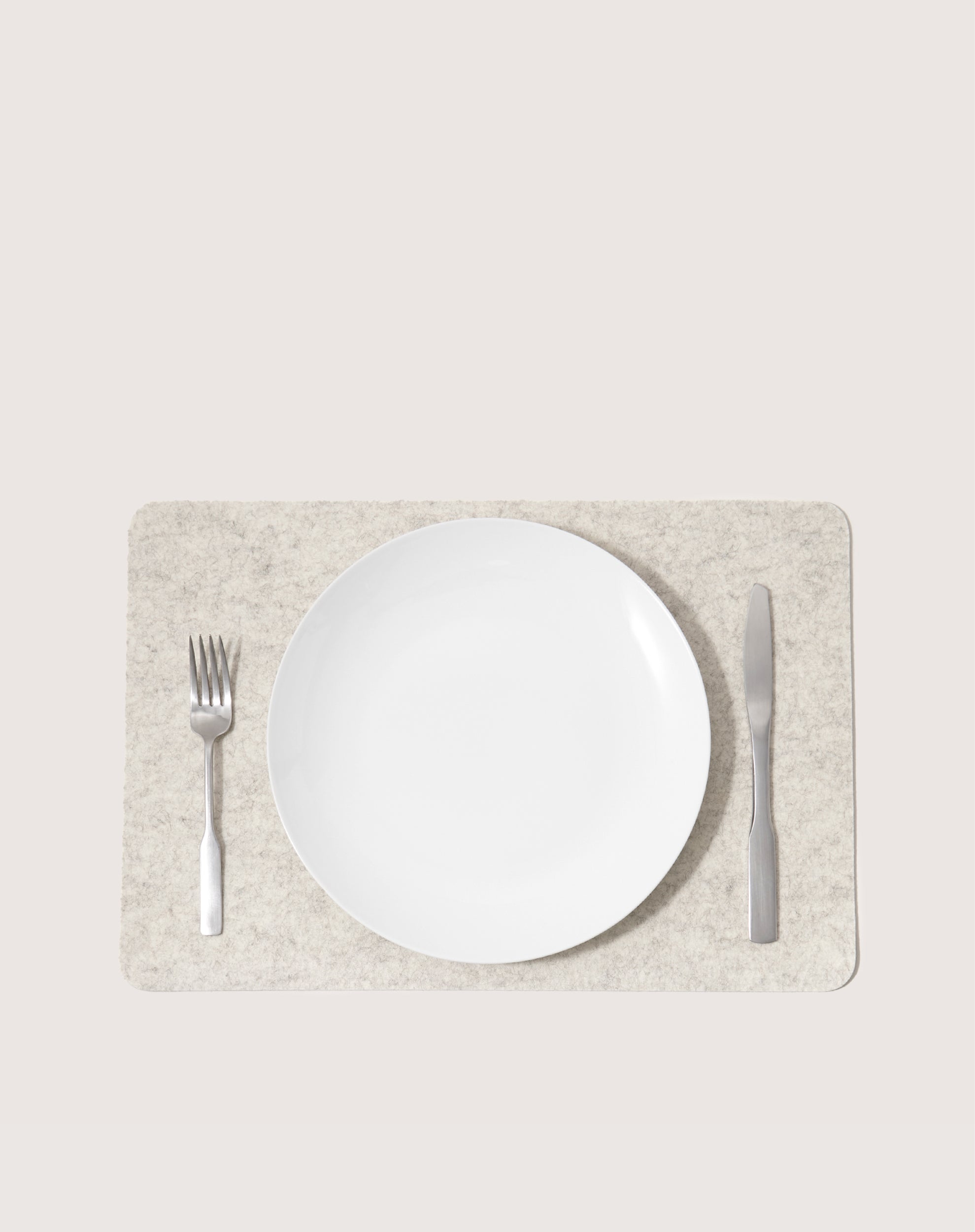 A white plate is centered on a light beige Merino wool placemat by graf lantz. A fork sits on the left and a knife on the right. The heat-resistant background complements this moisture-wicking setting flawlessly.