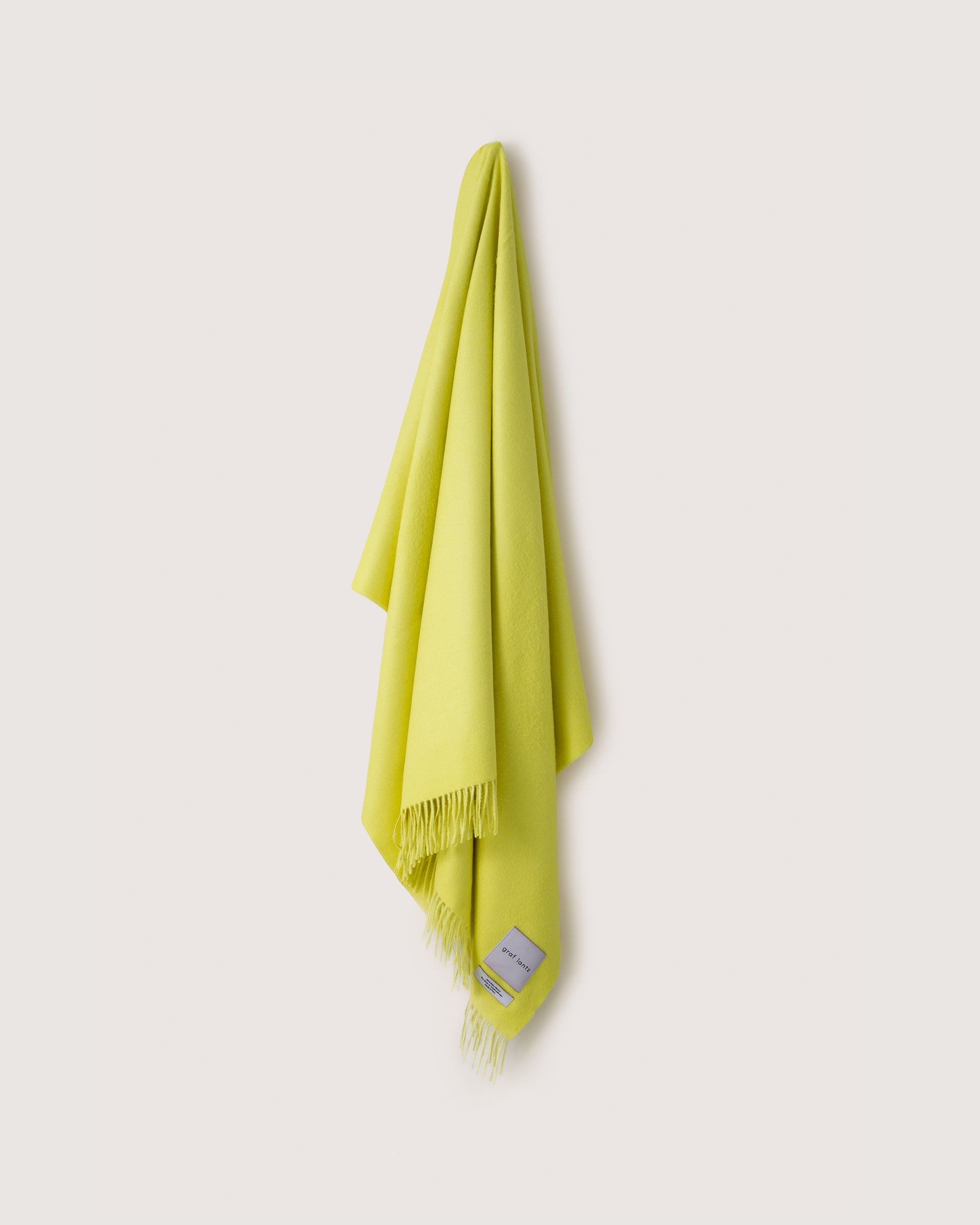A yellow Alpaca throw hanging on a wall hook, white background