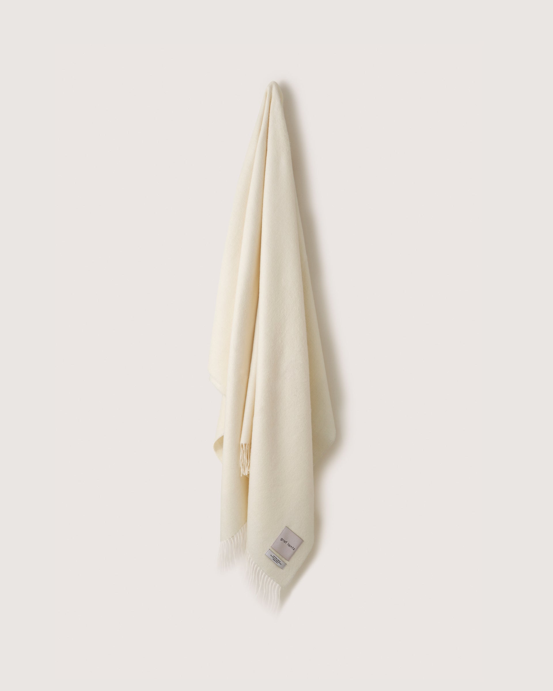 A white Alpaca throw hanging on a wall hook, white background