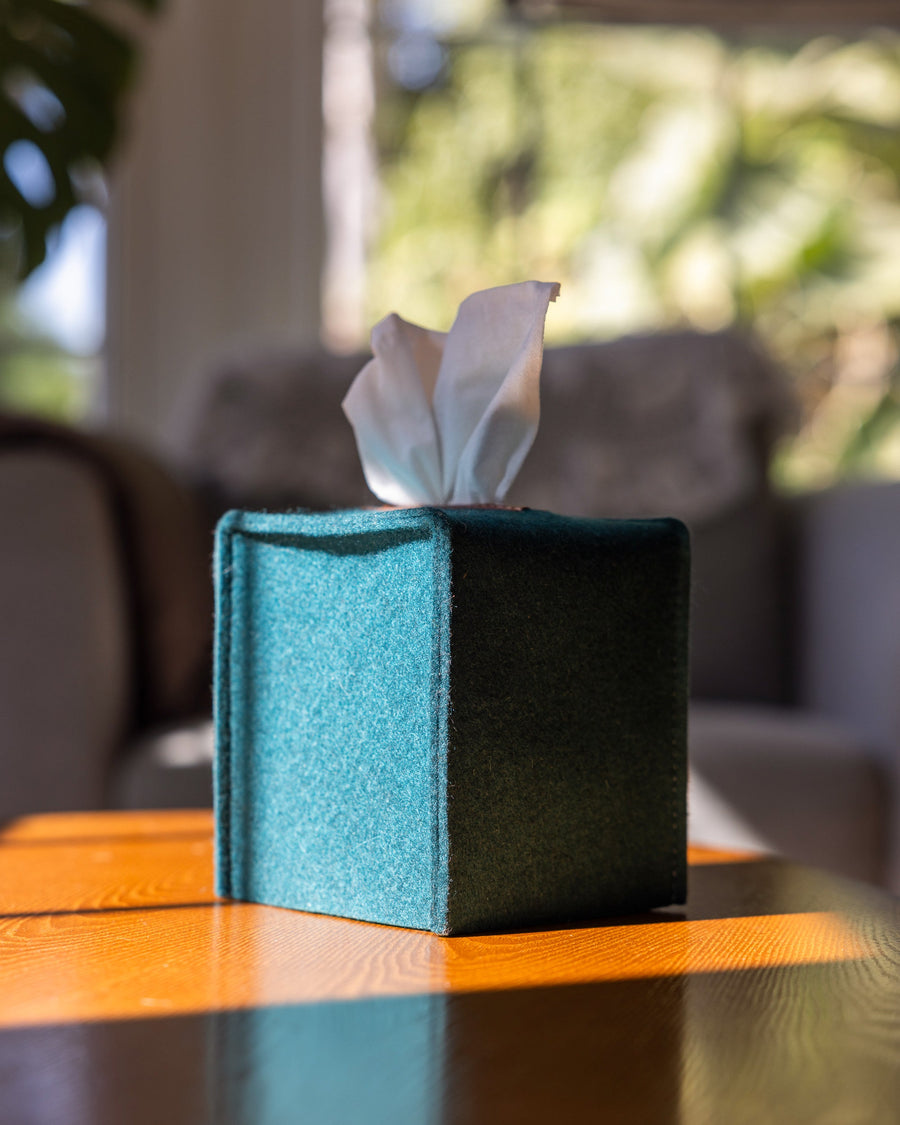 Kombu-colored Merino Wool Small Tissue Box Cover on a wooden couch desk, gray armchair in background